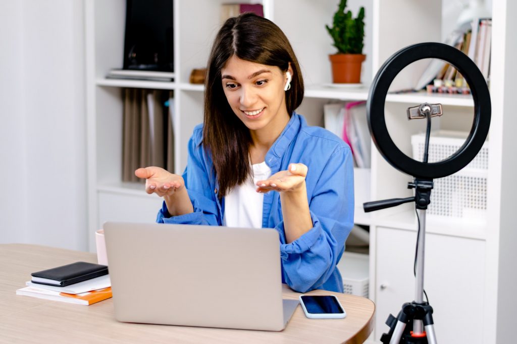 Girl blogger with earphones using laptop,chatting with followers in social network at home.
