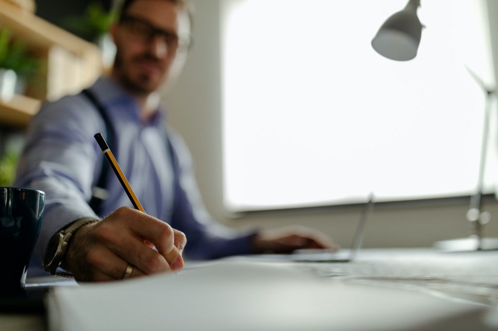 Interior designer is reviewing blueprints and holding pencil drawing on desk at home office.